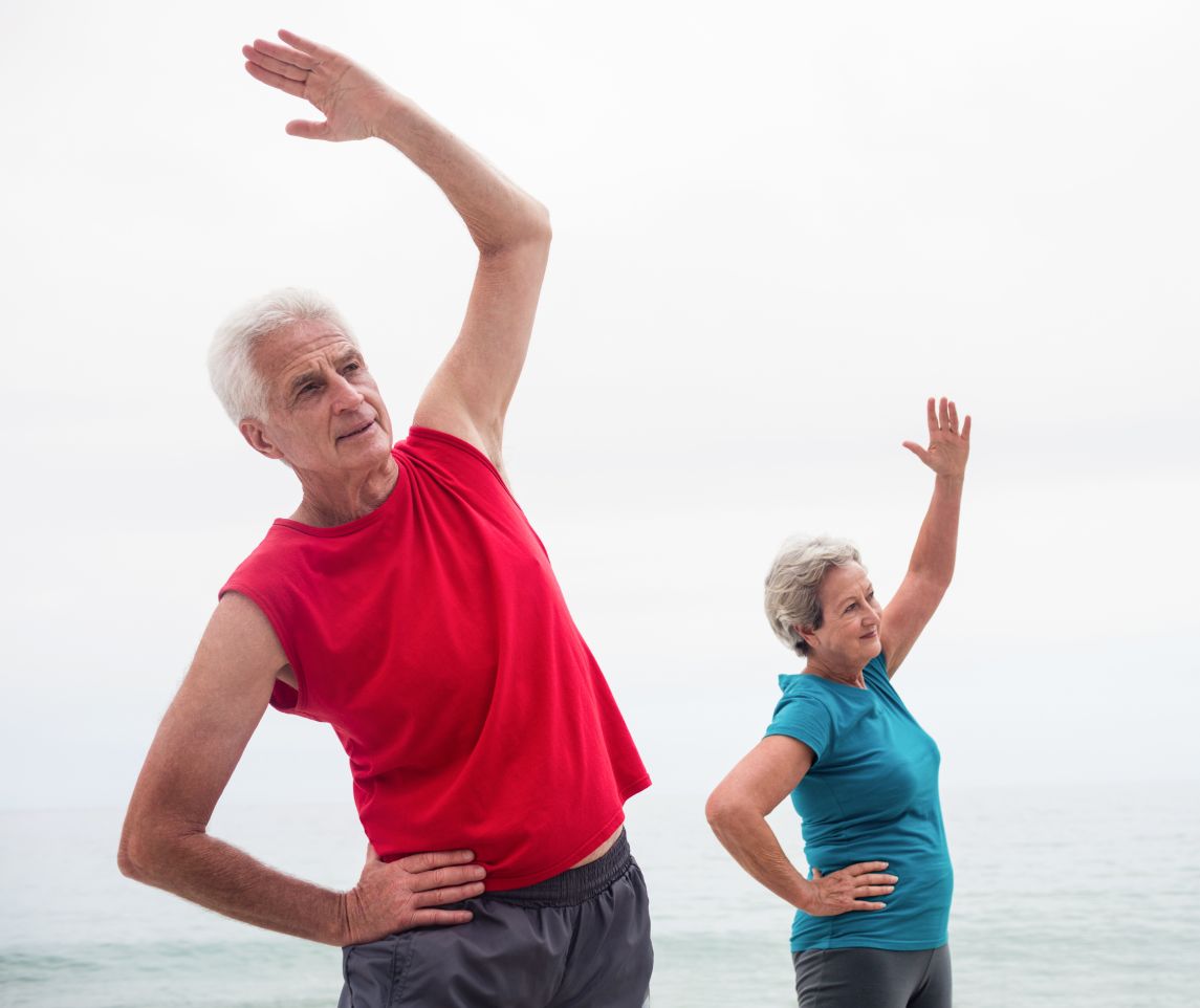 Senior couple performing stretching exercise on beach