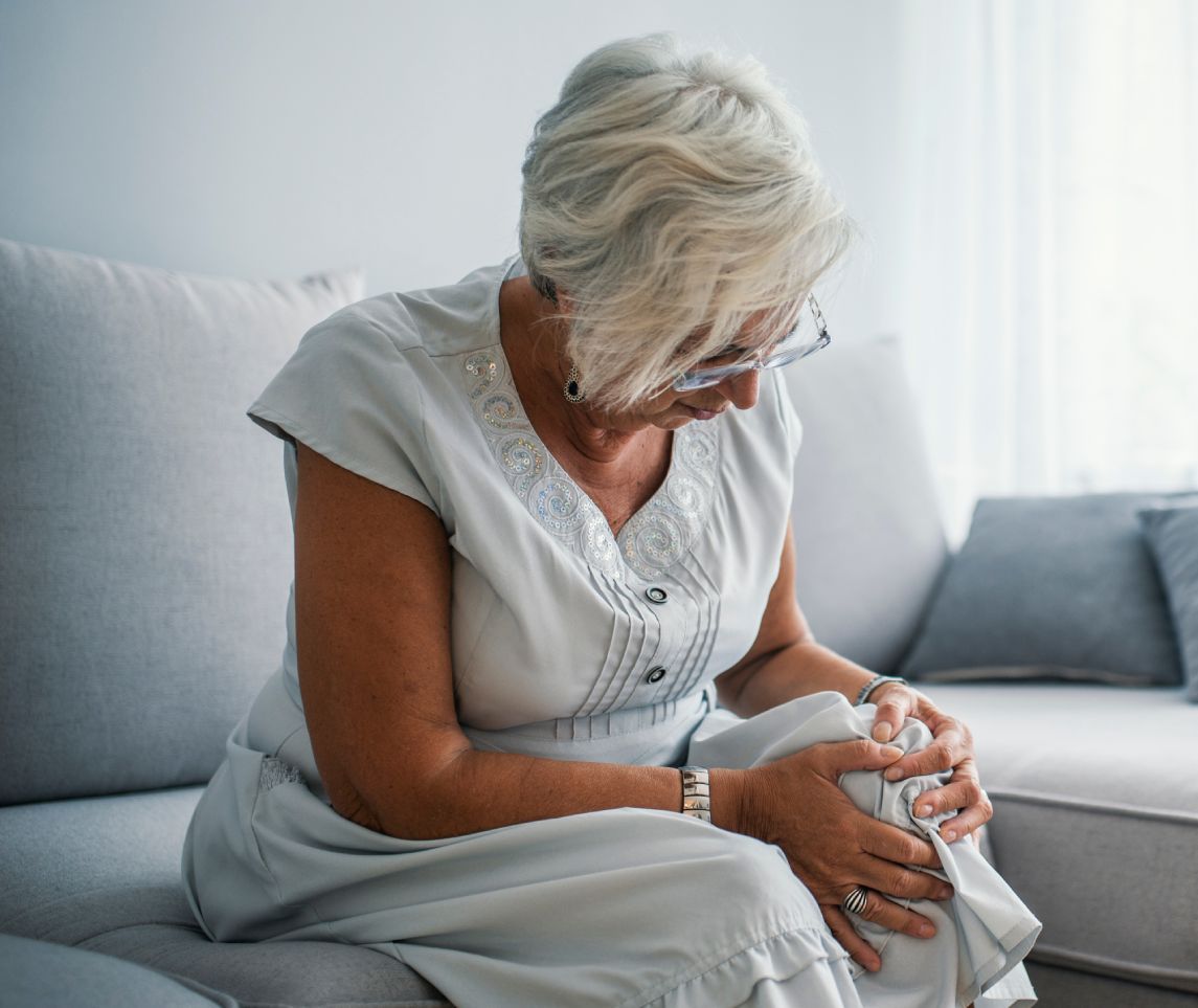 Senior woman holding the knee with pain. Old age, health problem and people concept - senior woman suffering from pain in leg at home. Elderly woman suffering from pain in knee at home