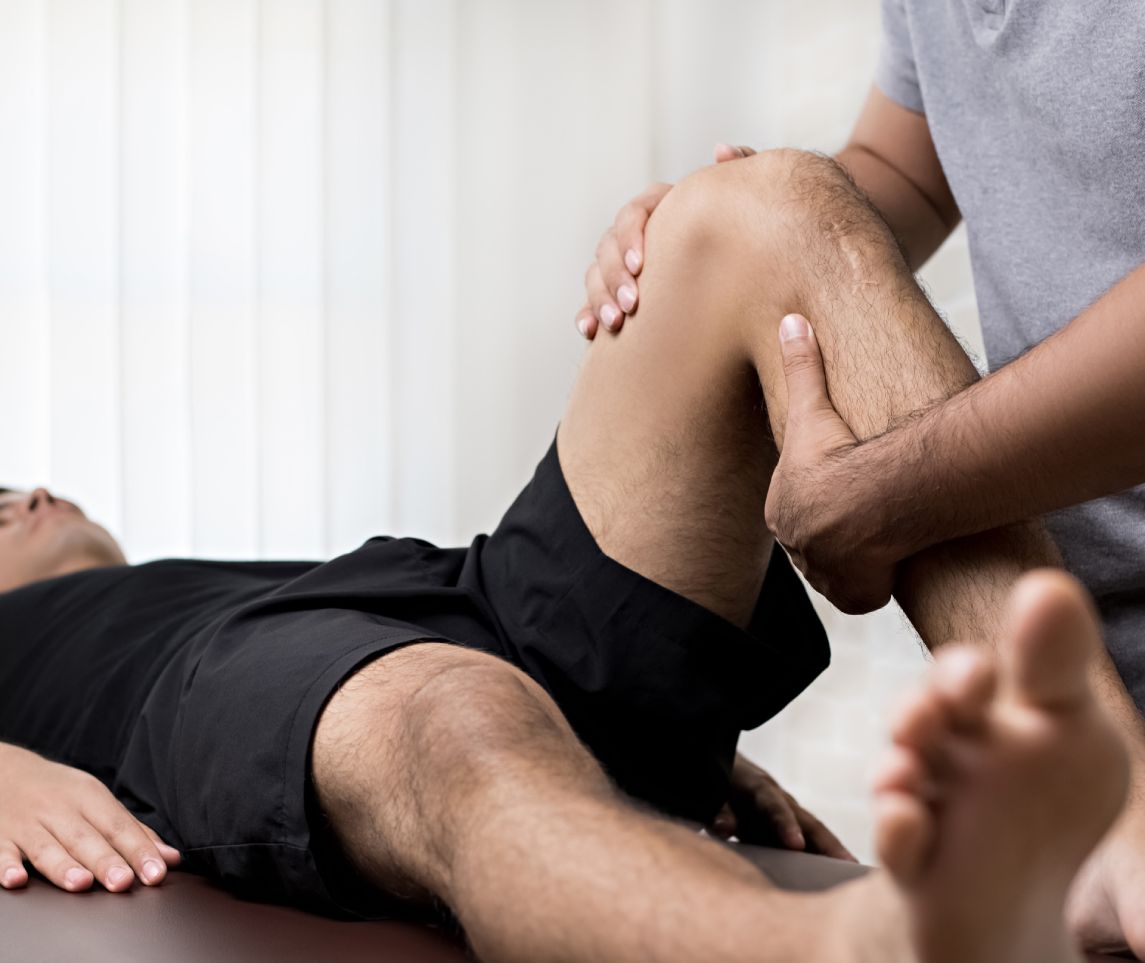 Therapist treating injured knee of athlete male patient in clinic - sport physical therapy concept