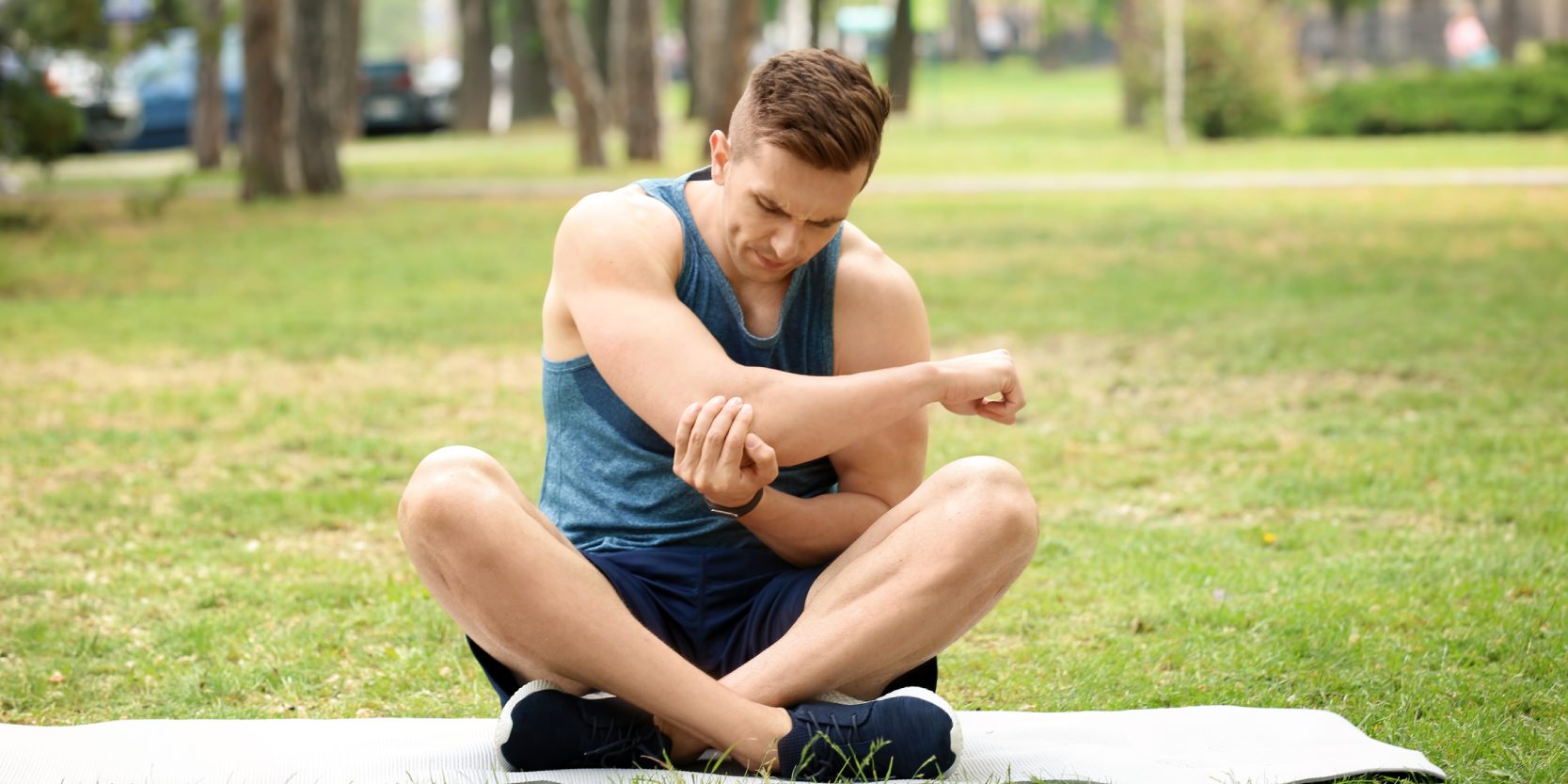 Male athlete suffering from elbow pain during training outdoors