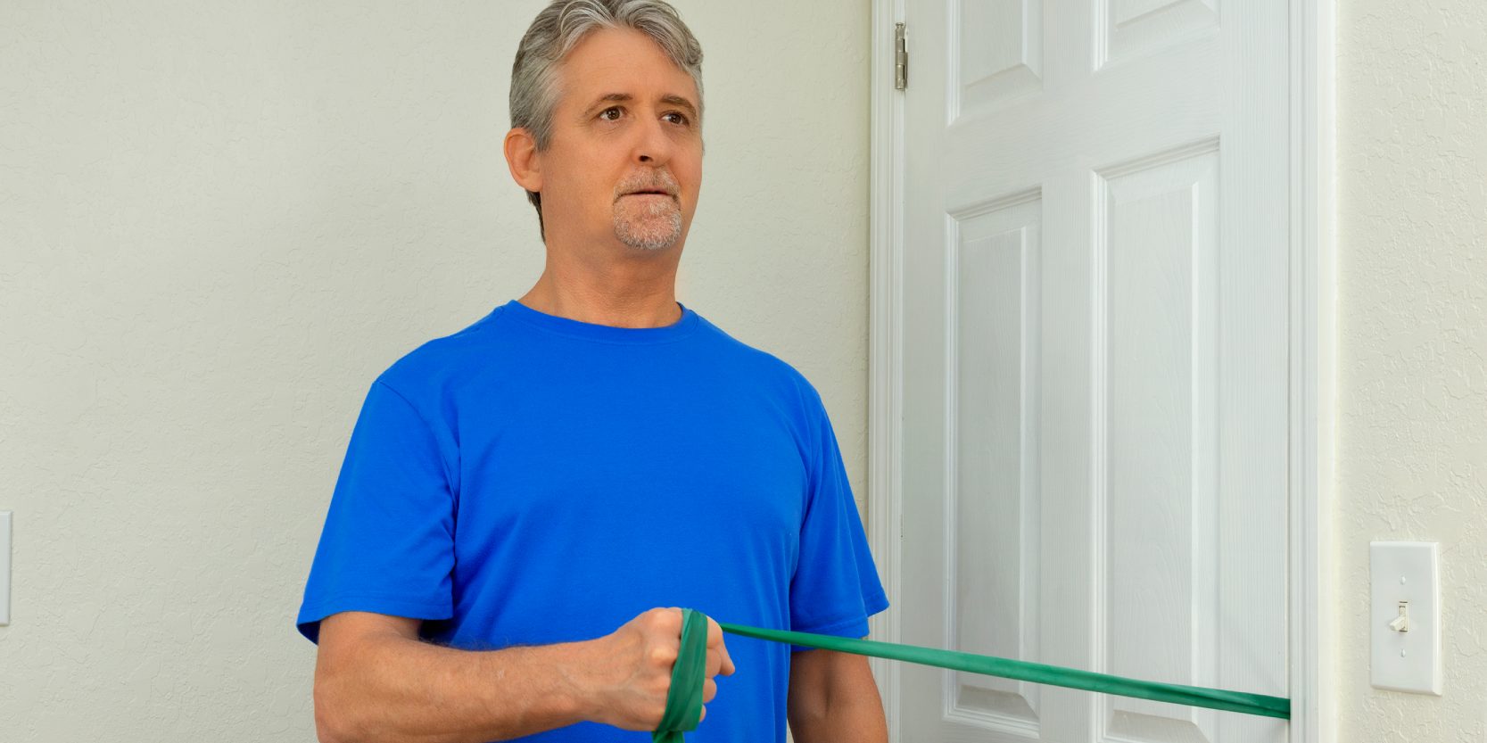 Middle age man doing shoulder surgery physical therapy with resistance rubber band exercises at home to strengthen the deltoid muscles to fully recover normal strength and flexibility.