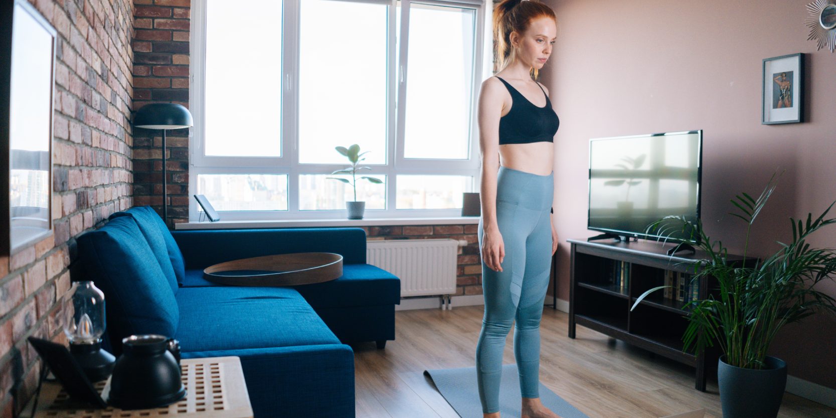 young woman doing stretching warm-up exercises for muscle at home. Concept of sports training red-haired lady during quarantine.