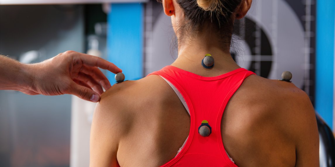 Technician placing markers on athletes shoulder, preparing for 3D gait or movement analyses