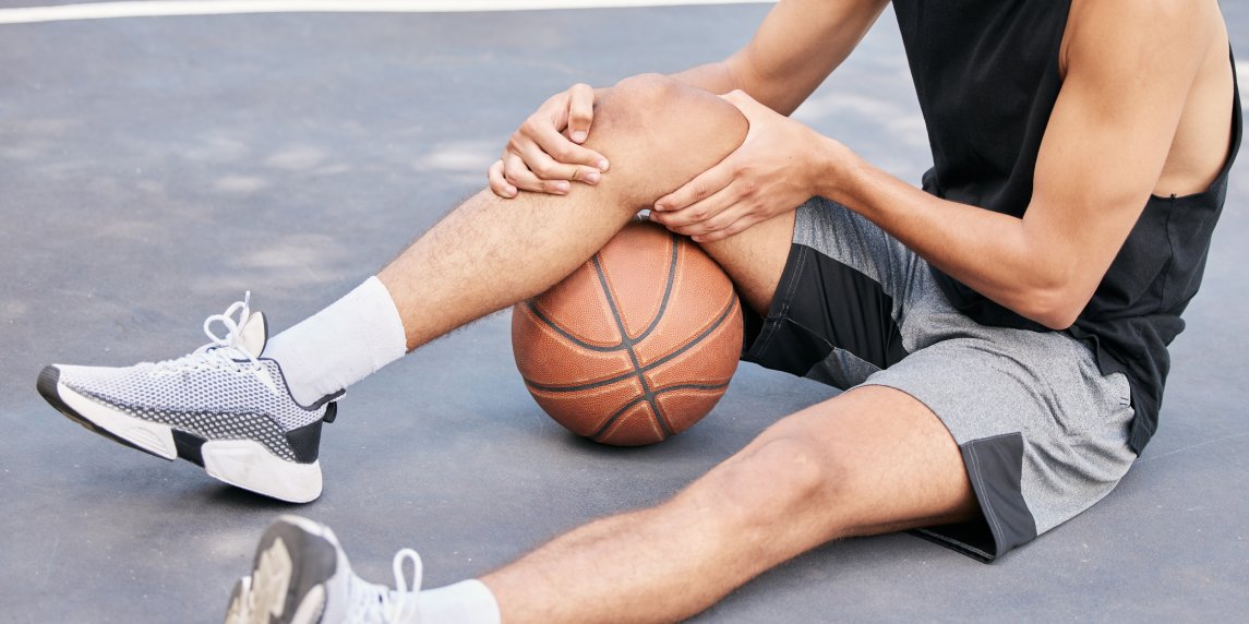 Basketball, man and knee in sports injury on the court holding painful, sore or tender area in the outdoors. Basketball player suffering from leg pain, joint or inflammation in sport match or game