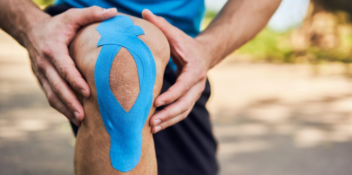 Close-up of male runner holding injured knee with kinesiology tape. Kinesiotaping concept