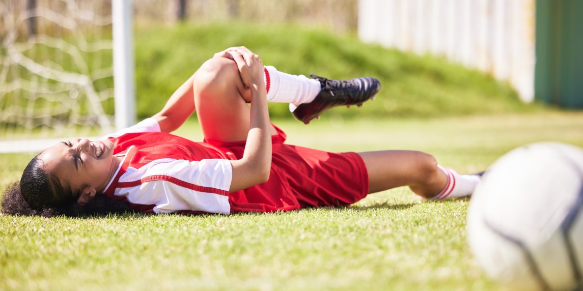Injured, pain or injury of a female soccer player lying on a field holding her knee during a match. Hurt woman footballer with a painful leg on the ground in agony having a bad day on the pitch