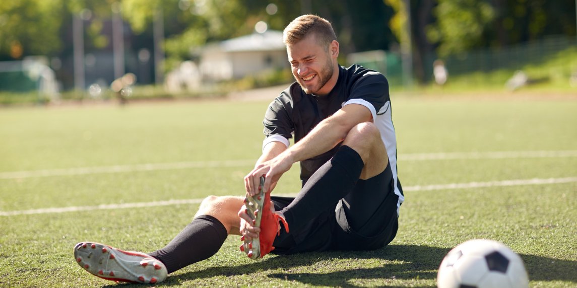 sport, football training, sports injury and people - injured soccer player with ball on field