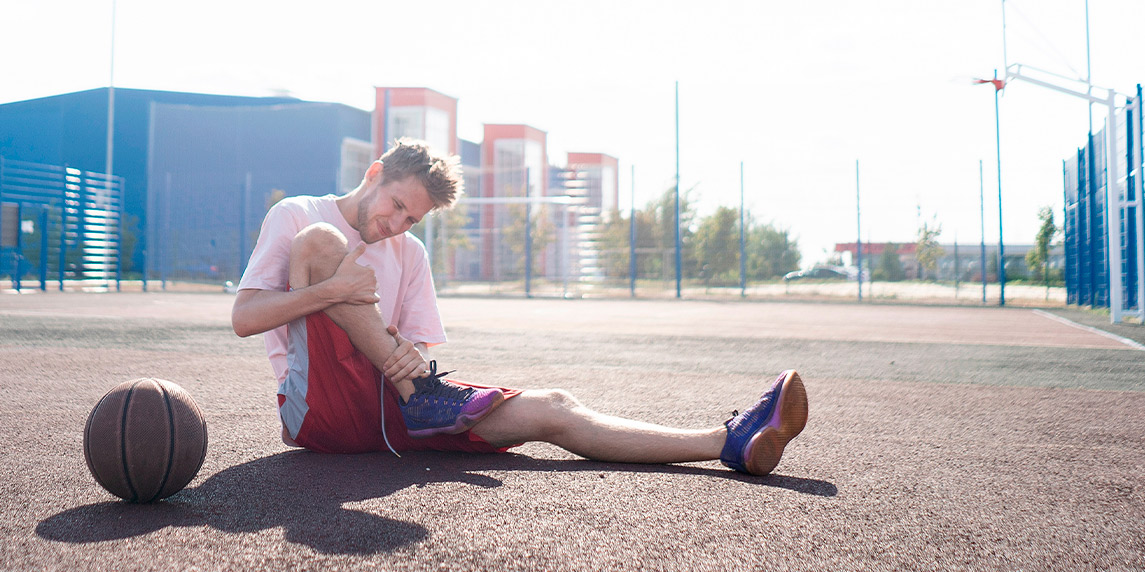 A man sitting on the ground with a leg brace, reflecting on the impact of basketball shoes on Achilles injuries.