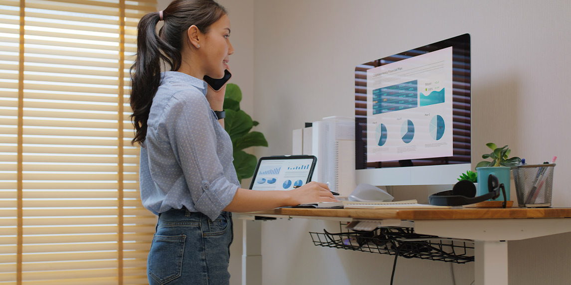 A woman stands at a desk with a computer and phone, promoting office wellness and ergonomic solutions in Santa Monica.