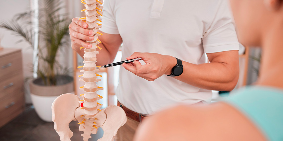 A man points with a pen at a spine model, demonstrating concepts for questions to ask a sports injury specialist.