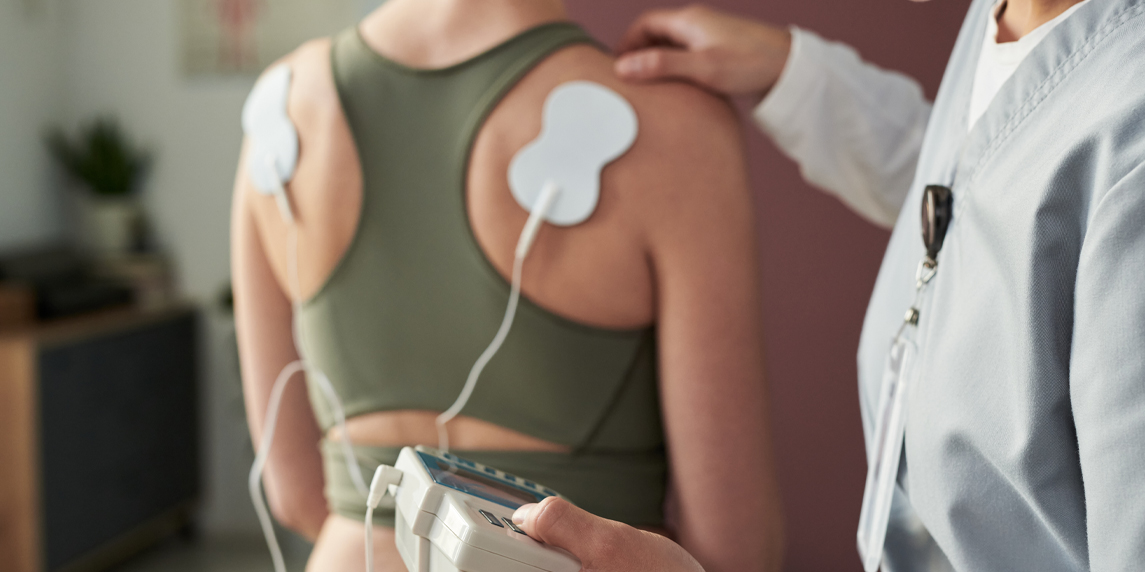 Physiotherapist conducting physical therapy session with patient using Neubie electronic device for muscle stimulation in medical setting