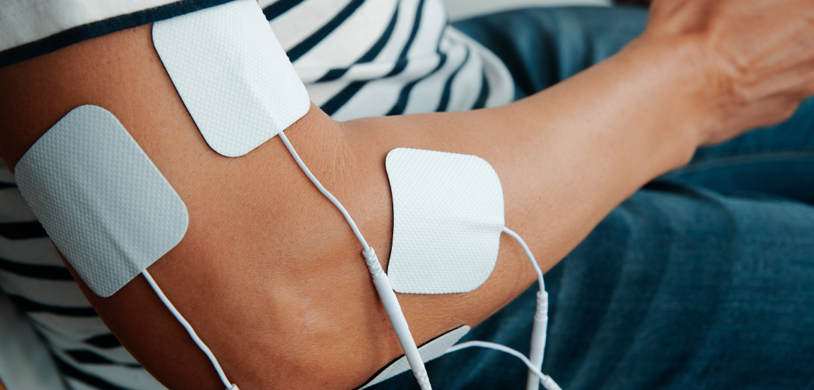 close view of a man sitting with electrode pads connected to an electrotherapy device for muscle recovery treatment